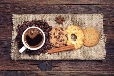 Cup of hot coffee and various sweet cookies on dark wooden table with burlap, top viewの写真素材