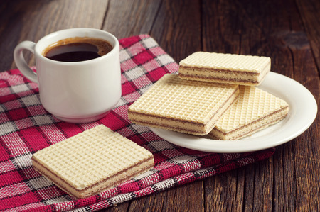 Wafers with chocolate and cup of hot coffee on wooden table, covert red tableclothの写真素材