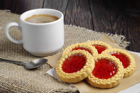 Cookies with jam and cup of hot coffee on burlap background