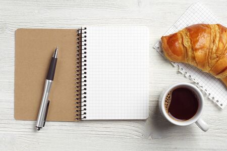 Notepad, pen, coffee cup and croissant on white wooden table, top viewの写真素材