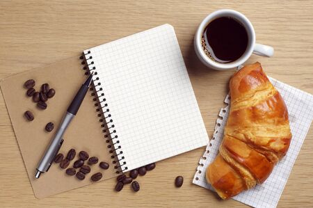 Opened notebook, coffee cup and croissant on desk, top viewの写真素材