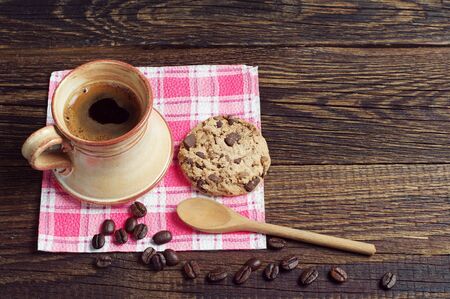 Cup of coffee and cookie with chocolate on a red napkin placed on a dark wooden tableの写真素材