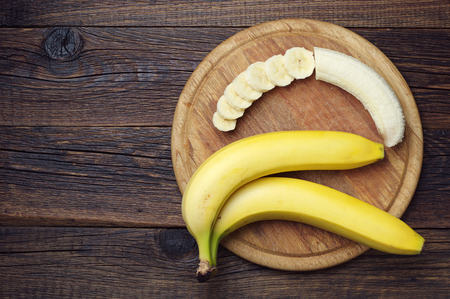 Ripe bananas and a sliced on wooden cutting board, top viewの写真素材