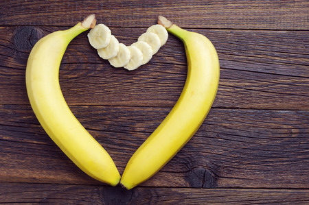 Bananas in shape of hearts on dark wooden table, top viewの写真素材