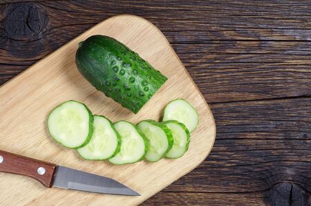 Green cucumber and slice on a cutting board on wooden background, top viewの写真素材