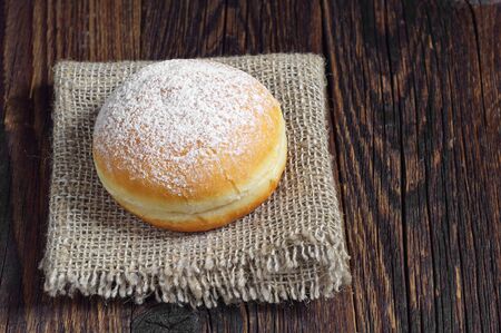 Sweet donut sprinkled with powdered sugar on old wooden table