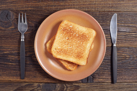 Toasted bread, fork and knife on dark wooden table, top viewの写真素材