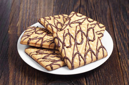 Plate with square chocolate cookies on dark wooden tableの写真素材