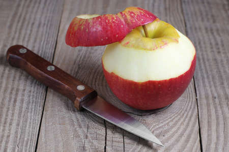 Peeled red apple and knife on rustic wooden tableの写真素材