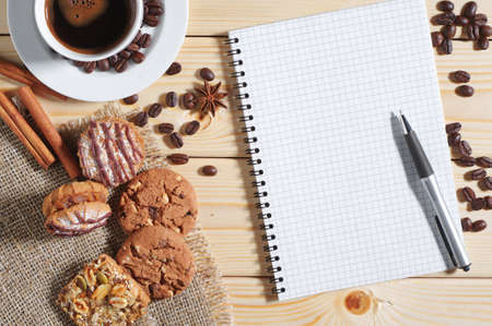 Cup of hot coffee, cookies and opened notepad on a wooden table, top viewの写真素材
