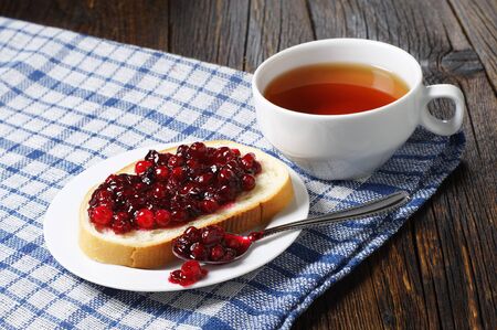 Slice of white bread with cranberry jam and a cup of hot tea in plate on old wooden tableの写真素材