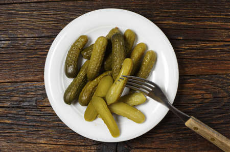 Small pickled cucumbers in plate and fork on old wooden table, top viewの写真素材