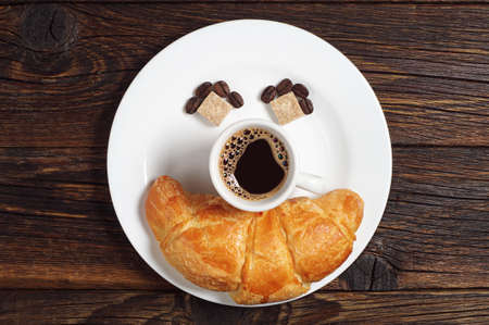 Cup of hot coffee with croissant in plate on old wooden table, top view