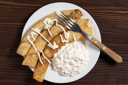 Homemade pancakes with cottage cheese and sour cream on dark wooden table, top view