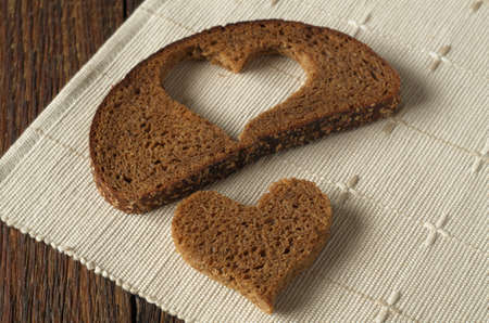 Black bread slices and a piece in shape of hearts on wooden table