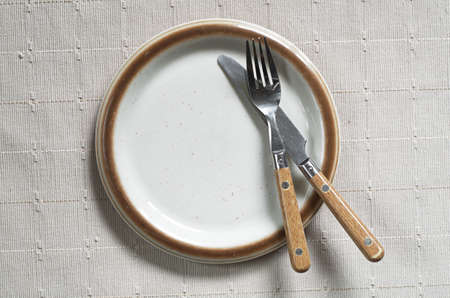 Empty old plate with fork and knife on tablecloth, top viewの写真素材