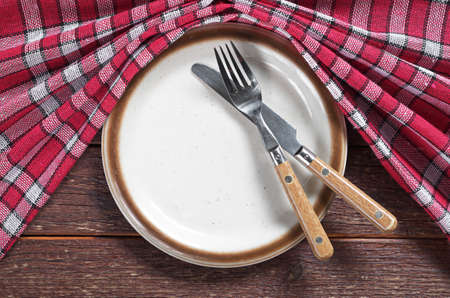 Empty old plate, fork and knife on wooden table with red tablecloth, top viewの写真素材
