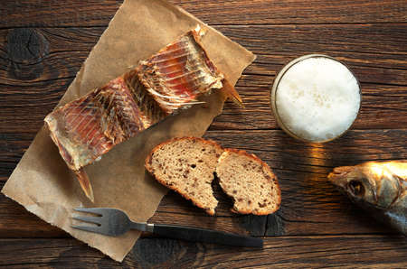 Salted fish on a paper and glass of beer on old wooden table, top view