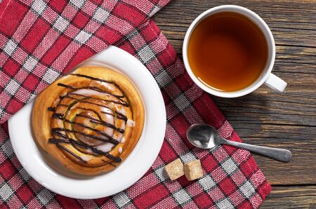 Cup of tea and sweet bun on wooden table with tablecloth, top viewの写真素材