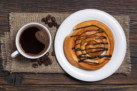 Cup of coffee and sweet bun on wooden table with burlap, top viewの写真素材