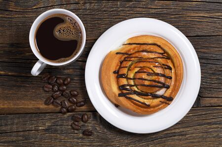 Sweet bun with chocolate and cup of coffee on old wooden background, top viewの写真素材