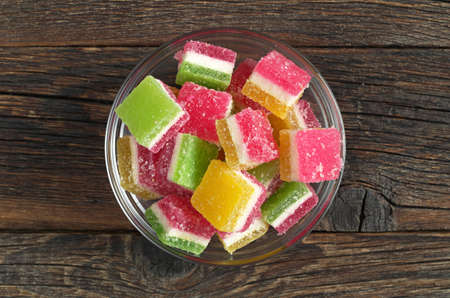 Candied fruit jelly in glass bowl on old wooden background, top view