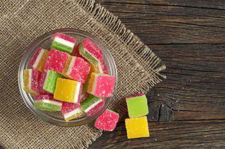 Colorful jelly candies in glass bowl on dark wooden background, top view