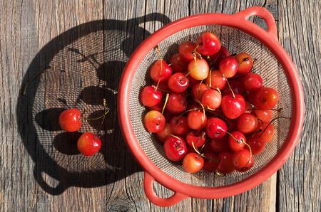 Cherries in a strainer on wooden background in the sunlight, top view