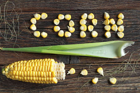 Grain in shape of word corn and cob on old wooden background, top view