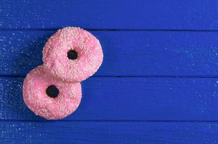 Two pink donuts on blue wooden background, top view. Space for textの写真素材