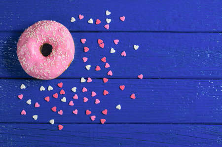 Pink donut on blue wooden background, top view