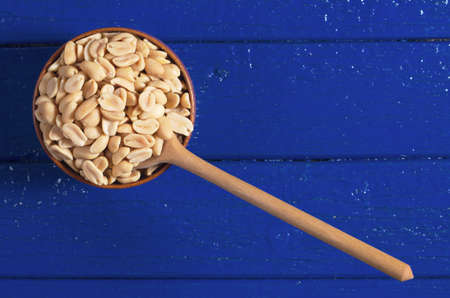 Roasted salted peanuts in bowl and near on blue wooden background, top view