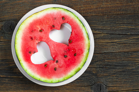 Round watermelon slice with cut in the shape of heart in plate on old wooden background, top viewの写真素材