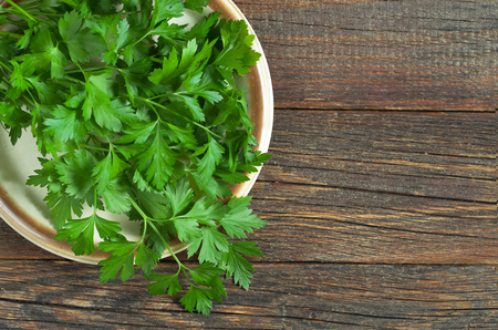 Fresh parsley in plate on wooden old background, top view. Copy spaceの写真素材