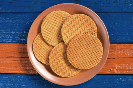 Round waffles with caramel in ceramic plate on colorful wooden surface, top viewの写真素材