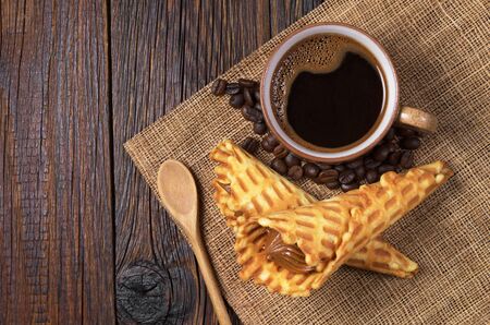 Cop of hot coffee and waffle cones with condensed milk on old wooden table, top viewの写真素材