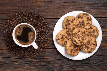 Cup of coffee, beans in shape of circle and cookies with chocolate in plate on dark wooden table, top viewの写真素材