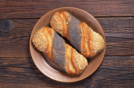 Buns with jam, sesame and poppy seeds in plate on dark wooden table. Top view