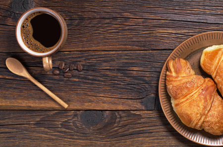 Cup of hot coffee and croissant on wooden background, top view. Space for textの写真素材