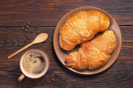 Cup of hot coffee and two croissants in plate on dark wooden table, top viewの写真素材