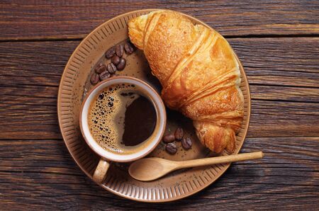 Cup of hot coffee and croissant in plate on dark wooden table, top viewの写真素材