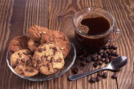 Cup of hot coffee and cookies with chocolate in plate for breakfast on old wooden table
