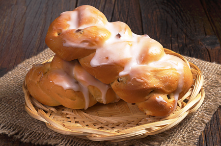 Two fresh buns with icing and raisins in plate on dark wooden tableの写真素材