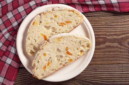 Two slices of ciabatta bread with dried apricot and pumpkin seeds in plate on wooden table, top view