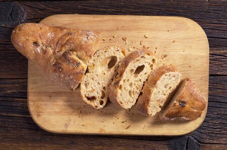 Sliced ciabatta bread with olives on wooden cutting board, top view