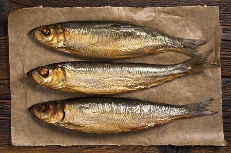 Smoked herring in paper on dark wooden table close up, top viewの写真素材