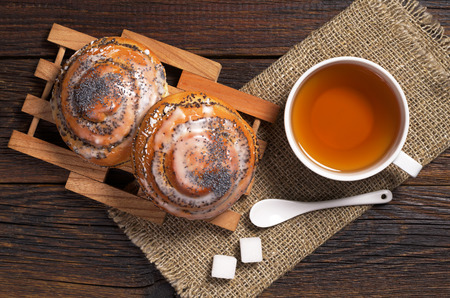 Two sweet buns with poppy seeds and cup of tea on dark wooden table, top viewの写真素材