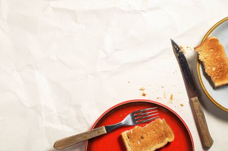 Slice of toasted bread in plate and cutlery on crumpled paper background, top view. Space for textの写真素材