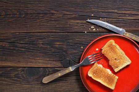 Slice of toasted bread in plate and cutlery on dark wooden background, top view. Space for textの写真素材