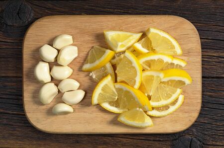 Peeled garlic and sliced lemon in plate on a wooden cutting board, top view. Healthy eatingの写真素材